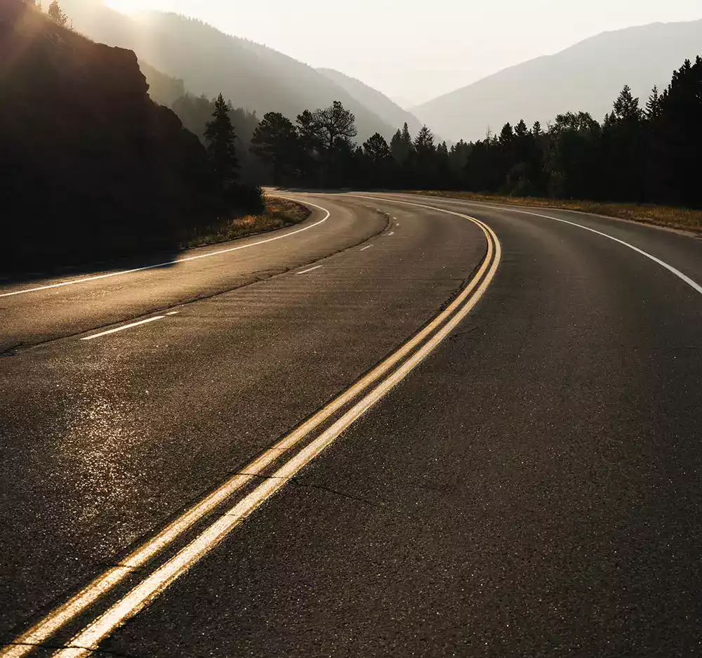 Route sinueuse en montagne au coucher du soleil, symbole de mobilité et de voyage.