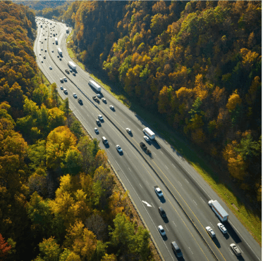geolocalisation-trafic-routier-gestion-flotte-ocean.jpg Vue aérienne d’une route traversant une zone boisée avec de nombreux véhicules circulant, illustrant le suivi et la gestion de flotte par géolocalisation.