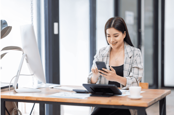 digitalisation-mobilite-entreprise-smartphone.png Femme au bureau utilisant un smartphone, illustrant la digitalisation et la gestion de la mobilité en entreprise.