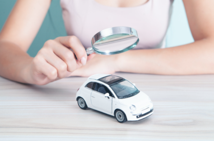 Personne observant une voiture miniature à la loupe, symbolisant la précision et le suivi offerts par la géolocalisation dans la gestion de flotte.