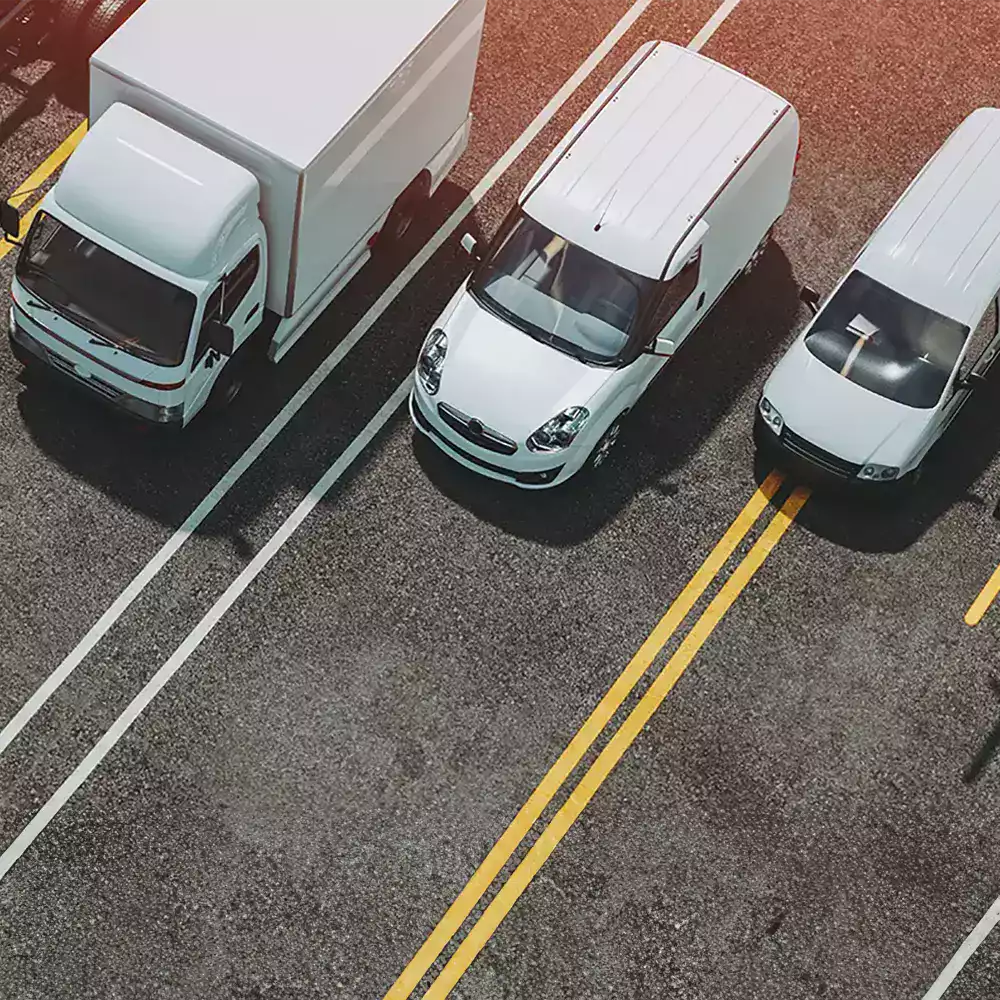 gestion-flotte-vehicules-utilitaires-ocean.webp Flotte de véhicules utilitaires alignés sur une route, symbolisant la gestion de flotte automobile d’entreprise.